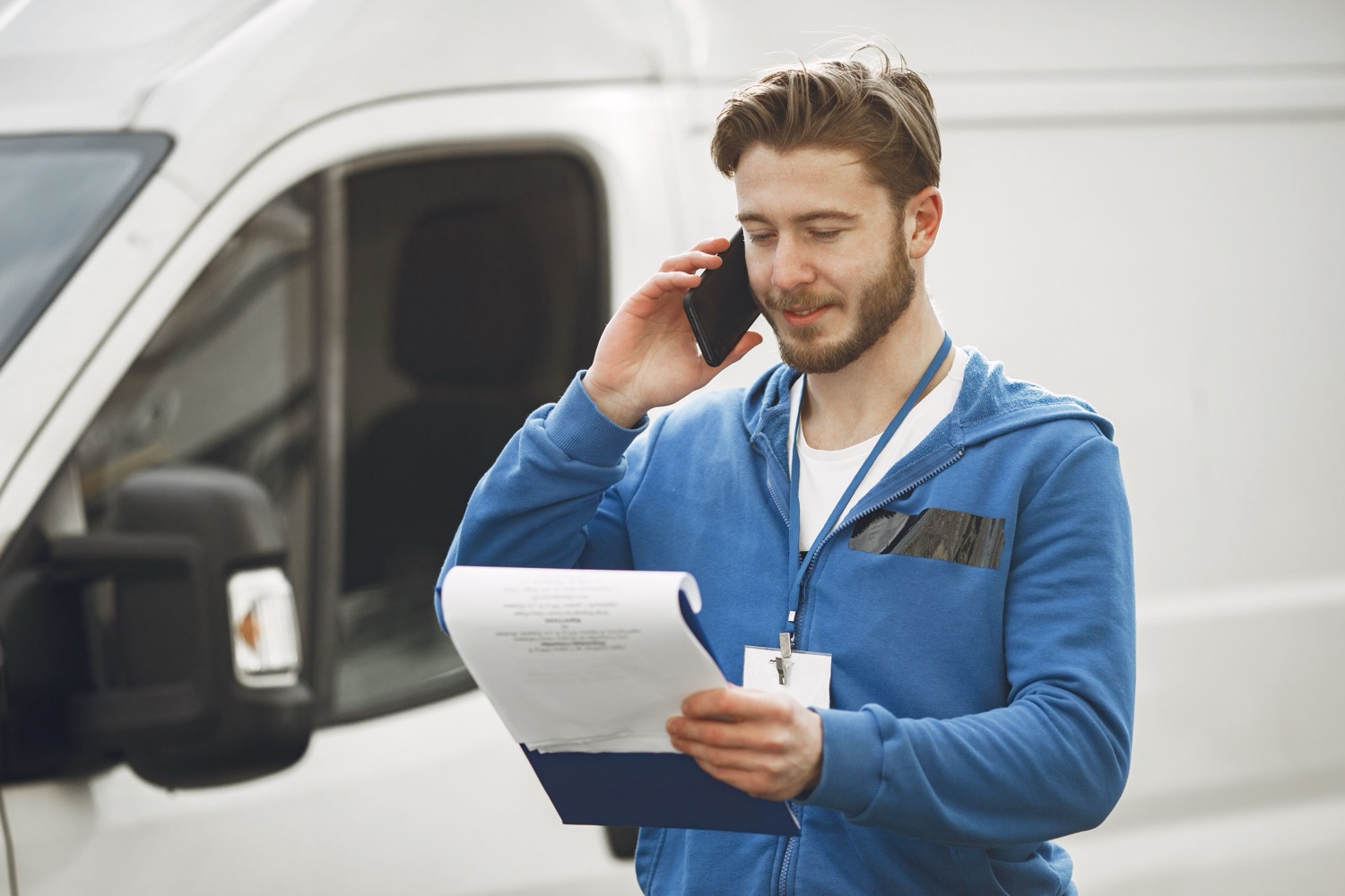 Mobile worker by a van using a phone and clipboard before a visit