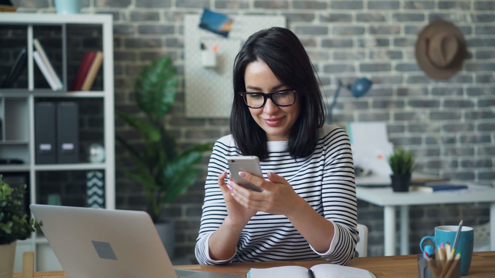Small business owner checking a smartphone beside her laptop and notebook