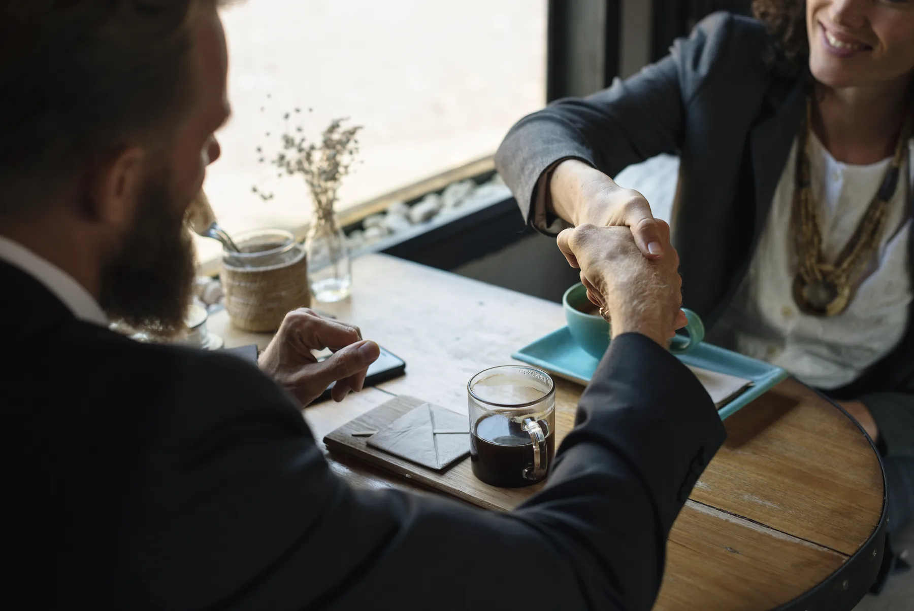 Two business people shaking hands across a cafe table after discussing an agreement