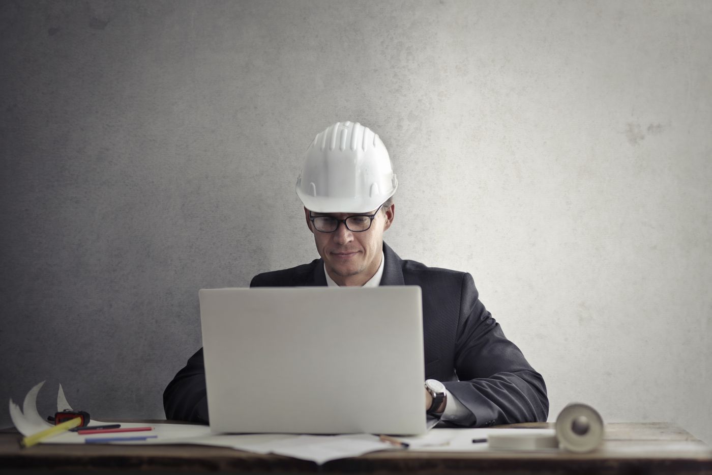 Engineer in hard hat using a laptop with work papers nearby