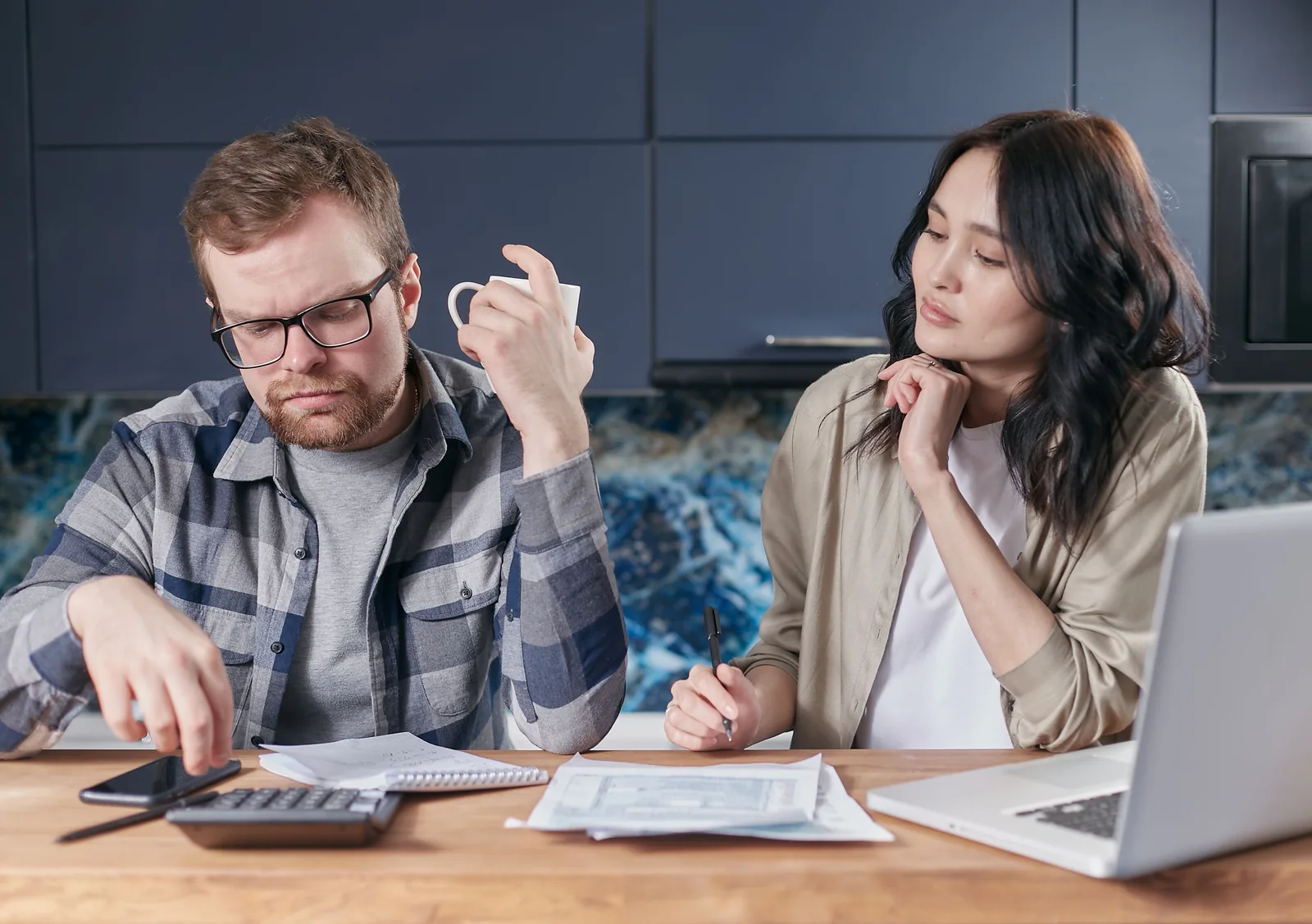 Two people reviewing small business paperwork with a calculator at a kitchen table