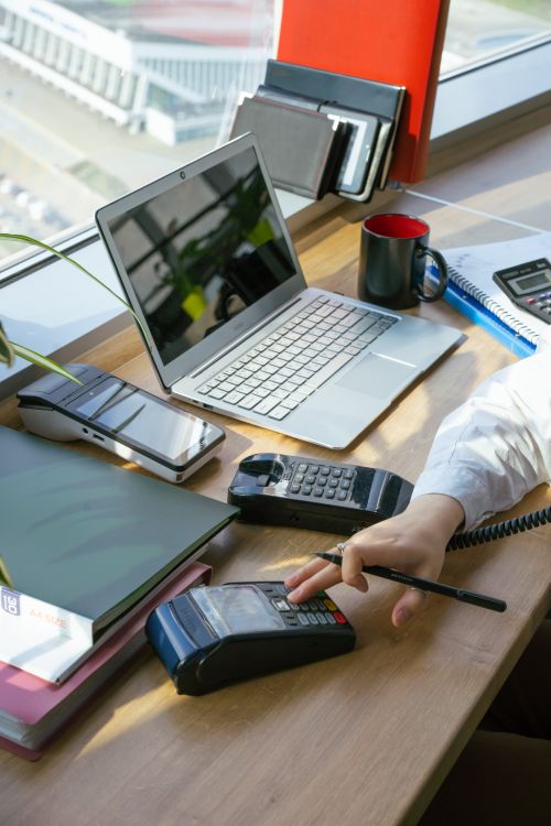 A person using a payment terminal at a desk with a laptop and papers
