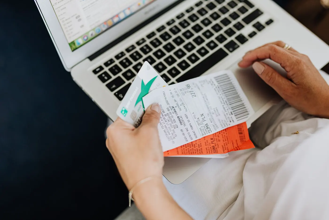Hands holding receipts and a payment card beside a laptop