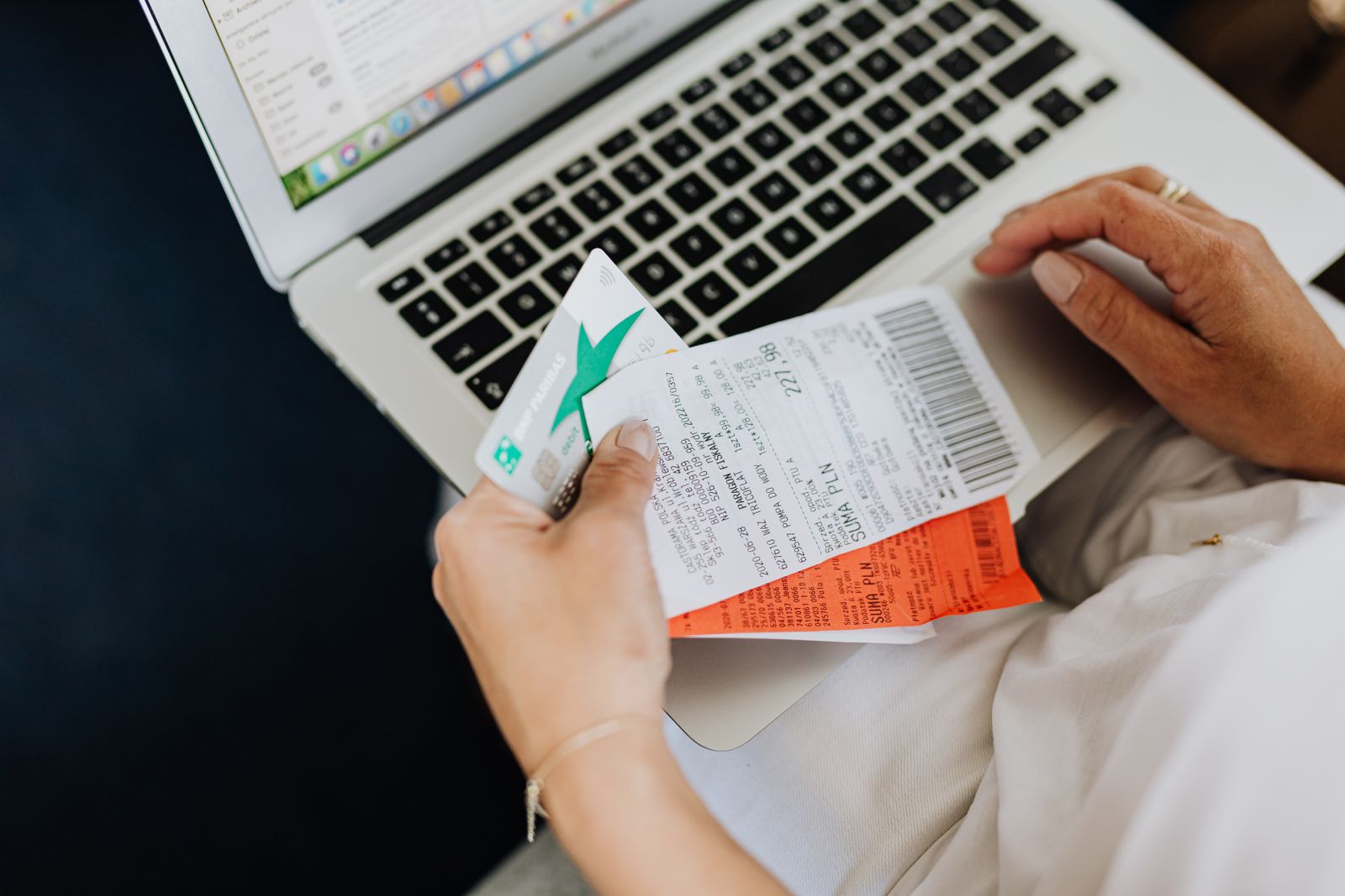 Hands holding receipts and a payment card beside a laptop