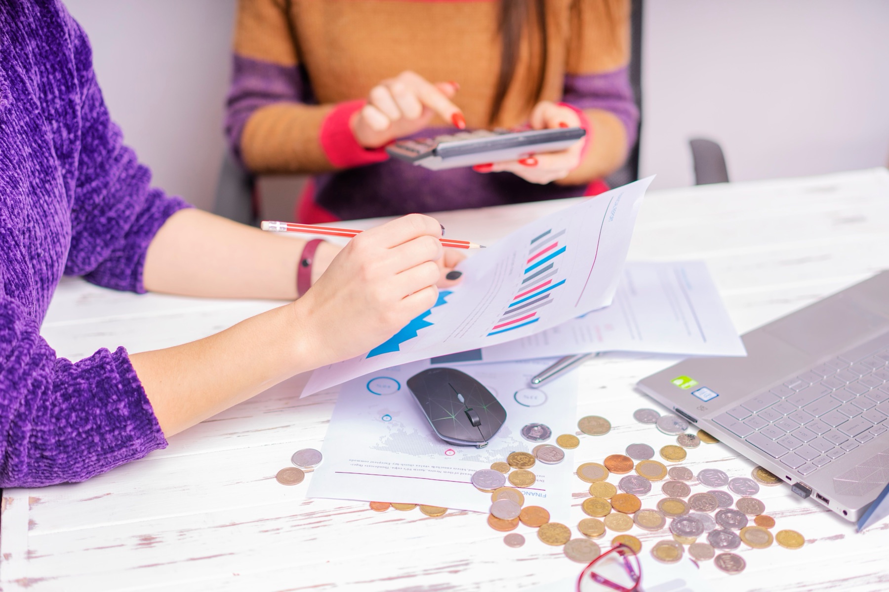 Two people reviewing business records with a calculator and loose coins on a desk