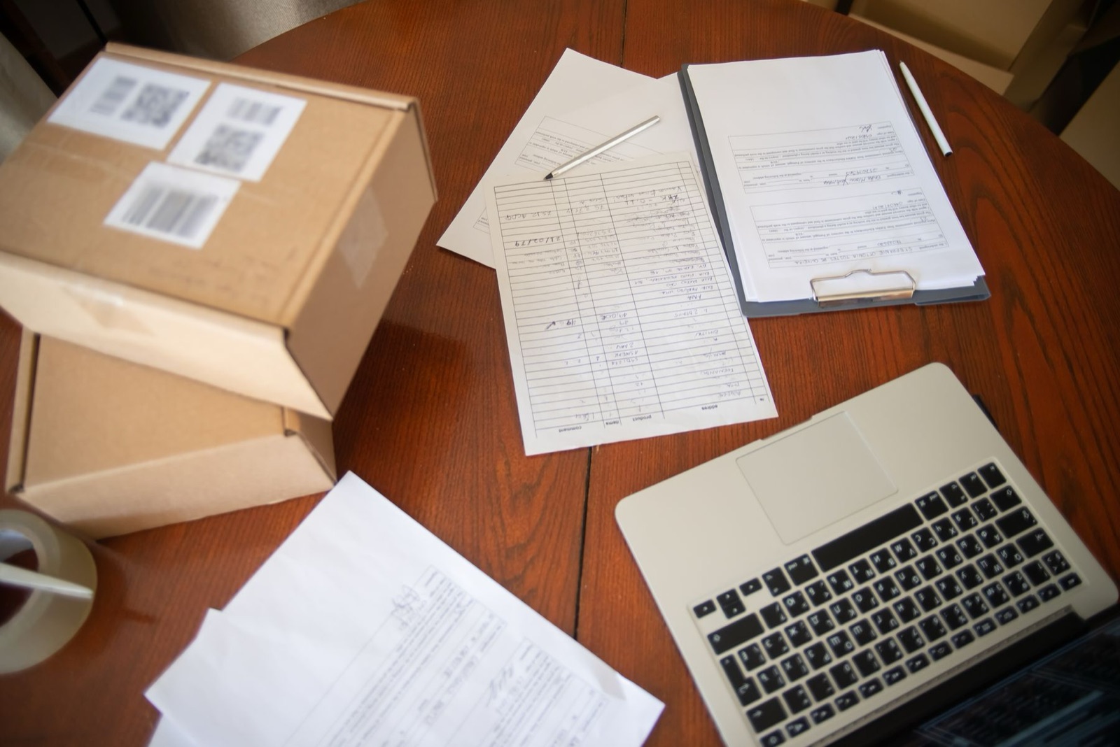 Laptop, parcel boxes and paper business records arranged on a wooden table