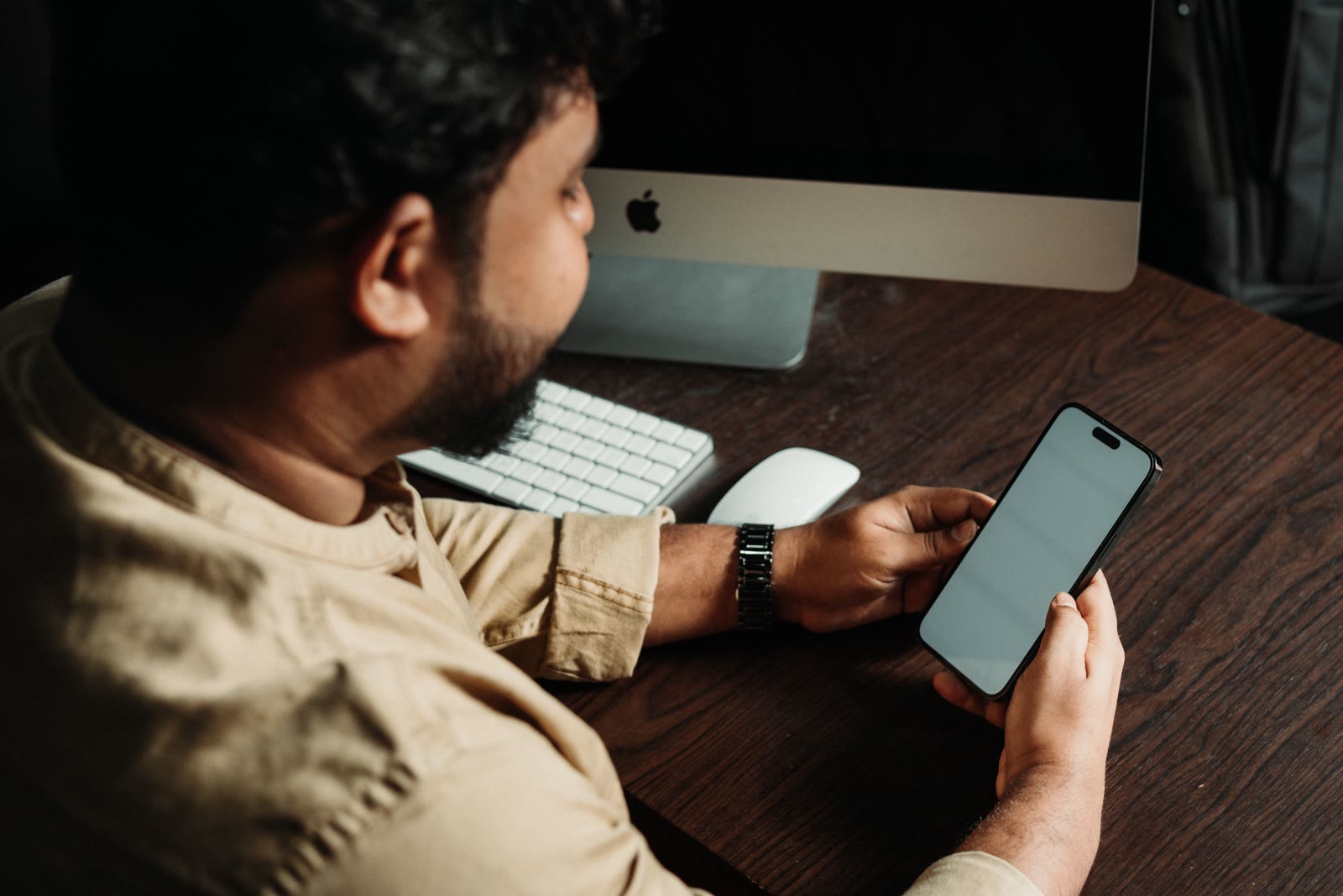 Business operator checking a smartphone beside a desktop computer